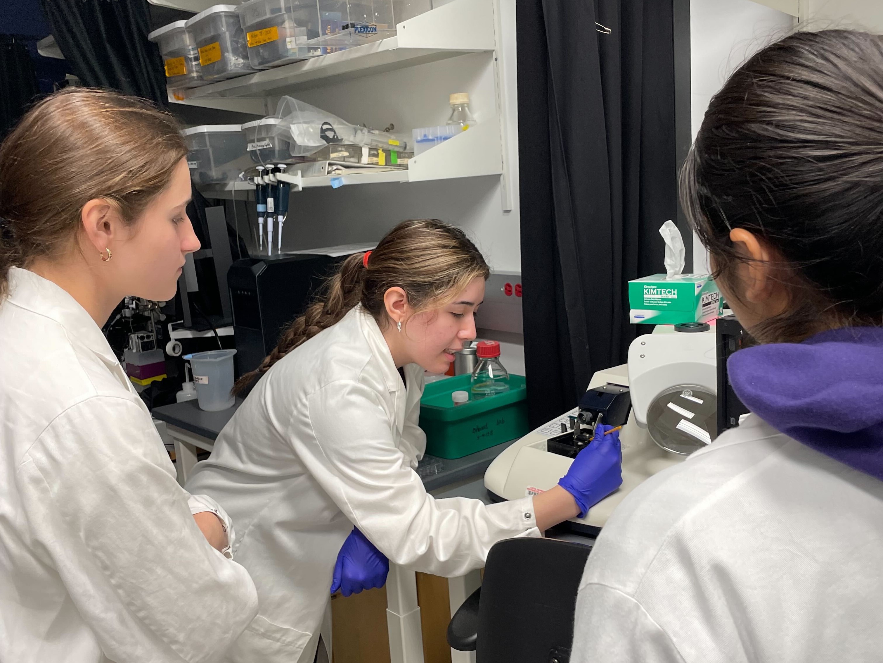 An intern demonstrates a technique for two other interns in the laboratory